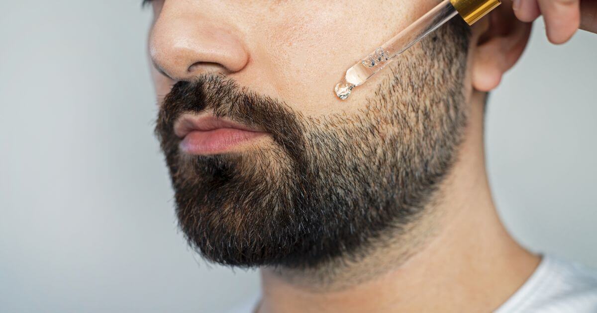 Man applying beard oil with dropper to groom and maintain facial hair, showcasing proper beard care technique.