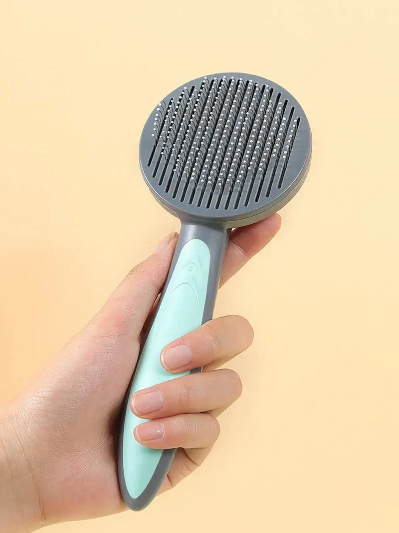 Hand holding a self-cleaning pet grooming brush with ergonomic handle, ideal for cats, dogs, and rabbits.