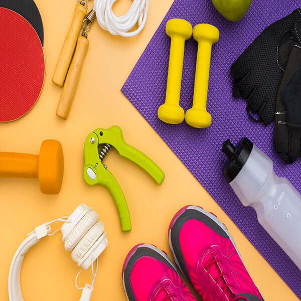 Assortment of fitness equipment on a colorful background, including pink sneakers, yellow dumbbells, a grip strengthener, and headphones